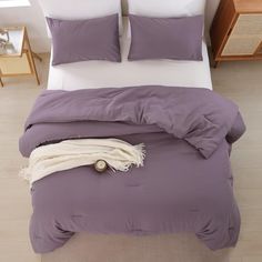 a bed with purple sheets and white pillows