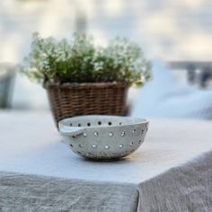 a white bowl sitting on top of a table next to a basket filled with flowers