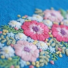 a close up view of some flowers on a blue cloth with yellow and pink thread