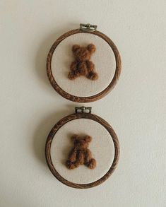 two cross stitch teddy bears are hanging on the wall behind hoop frames that have been embroidered onto them