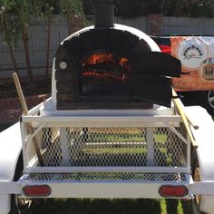 an outdoor pizza oven sitting in the back of a white truck parked on top of a grass covered field