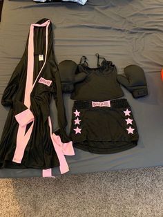 a bed topped with black and pink clothing on top of a gray sheet covered floor