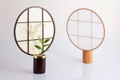 two round mirrors sitting next to each other on top of a white table with a plant in it