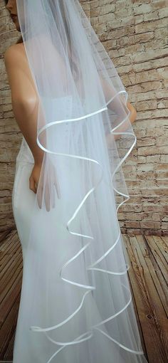 a woman in a wedding dress with a veil on her head is standing next to a brick wall