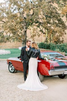 a bride and groom standing next to a red car