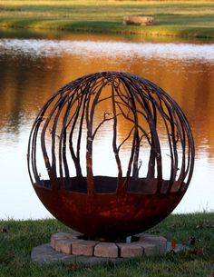 a large metal sculpture sitting on top of a lush green field next to a lake