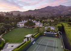 an aerial view of a tennis court surrounded by greenery and mountains in the background