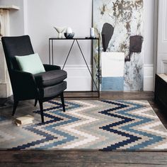 a black chair sitting on top of a wooden floor next to a white and gray rug