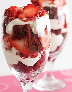 two glasses filled with strawberries and cream on top of a pink tableclothed surface