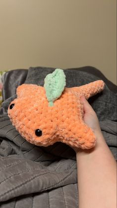 a hand holding an orange stuffed animal with a green leaf on it's head