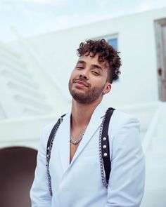 a man with curly hair wearing suspenders and a white shirt is standing in front of a building