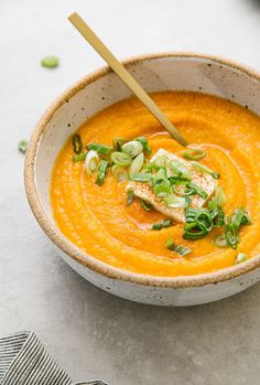 a bowl filled with carrot soup and topped with green onions