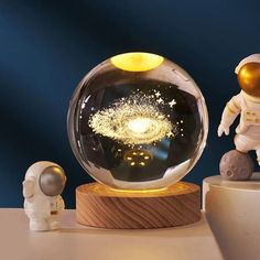 an astronaut figurine next to a glass ball with fireworks in it on a table