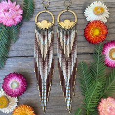 two pairs of earrings sitting next to flowers on top of a wooden table with daisies