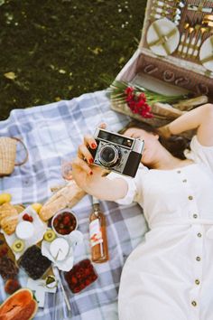 a woman laying on a blanket holding a camera in front of food and drink bottles