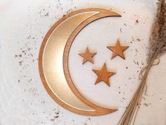 three wooden stars and a crescent on a white tablecloth with dried grass next to it