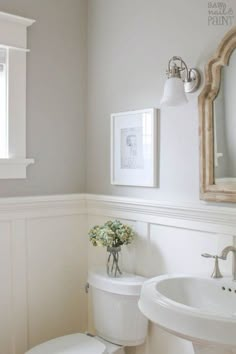 a white toilet sitting next to a sink in a bathroom under a framed painting on the wall