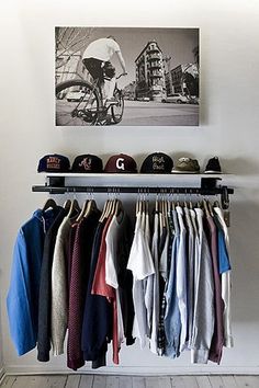 a rack with hats and shirts hanging from it's sides in front of a painting