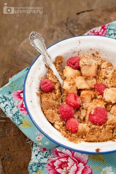 a bowl filled with cereal and raspberries on top of a floral table cloth