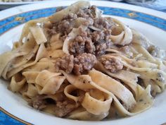 a white plate topped with pasta covered in meat and sauce on top of a table