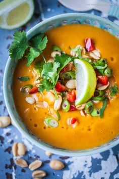 a white bowl filled with soup and garnished with cilantro, lime, cashews, and peanuts