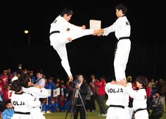 two men in white uniforms doing tricks on a tripod while people watch from the sidelines