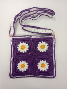 a purple crocheted purse with white and yellow flowers