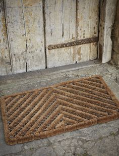 a door mat sitting on the ground next to a wooden door with rusted metal bars