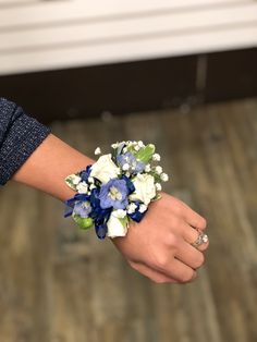 a woman's hand holding a blue and white wrist corsage with flowers