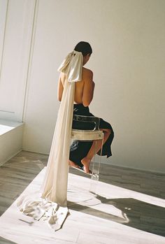 a woman sitting on top of a chair next to a white wall and wearing a black dress