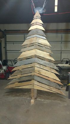 a large wooden christmas tree made out of pallet wood in a garage with lights on