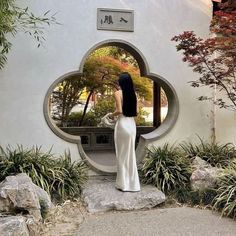 a woman standing in front of a circular mirror on the side of a white building