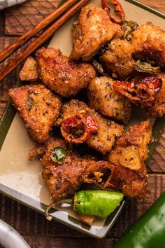 chicken wings with peppers and chopsticks on a plate next to a green pepper