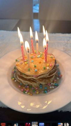 a stack of pancakes with lit candles on top of it in front of an iphone