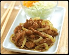 a white plate topped with meat and onions next to a bowl of coleslaw