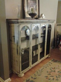 an old china cabinet with glass doors in a living room area next to a painting on the wall