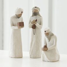 three figurines are sitting on a table with one holding a book and the other reading