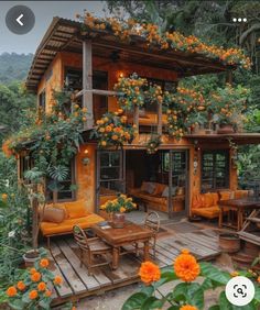 an orange house with lots of flowers on the roof and windows above it is surrounded by greenery