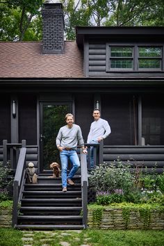 two men sitting on steps in front of a house with their dog and another man standing next to them