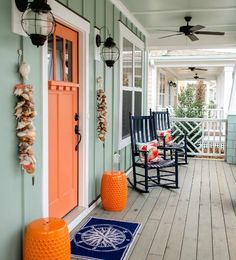 two rocking chairs on the front porch of a house with an orange door and blue rug