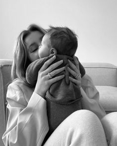 a woman sitting on a couch holding a baby in her lap and kissing it's face