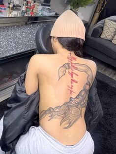 a woman sitting on the floor with her back turned to the camera and tattoos on her body