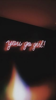 a neon sign that says you go girl on the side of a wall in a dark room