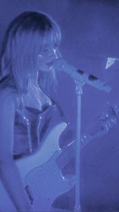 a woman with blonde hair playing guitar in front of a microphone and microphone mic on stage