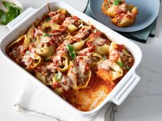 a casserole dish with meat and cheese on the side next to a plate of pasta