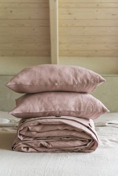 three pillows stacked on top of each other in front of a bed with pink sheets