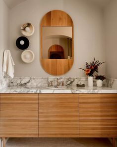 a bathroom with marble counter tops and wooden cabinetry, along with an oval mirror above the sink