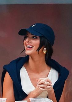 a woman sitting at a table wearing a hat and holding her hands together while smiling