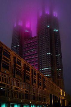 two tall buildings lit up at night with fog in the air and lights on them