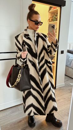 a woman is taking a selfie while wearing a zebra print coat and black boots